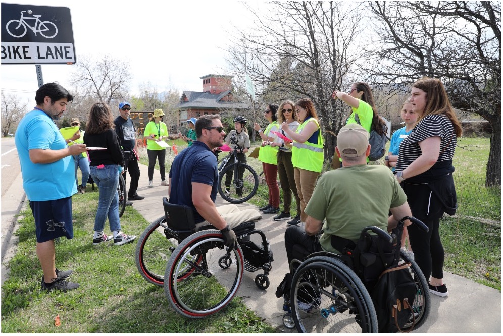 Bike and roll auditors stand on a sidewalk or sit in wheelchairs and talk amongst themselves
